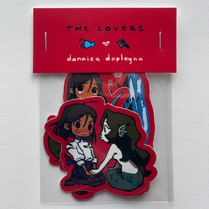 May include: A pack of stickers with illustrations of two characters, one human and one mermaid, holding hands. The stickers are on a red card with the text "THE LOVERS" and "dannica doplayna".