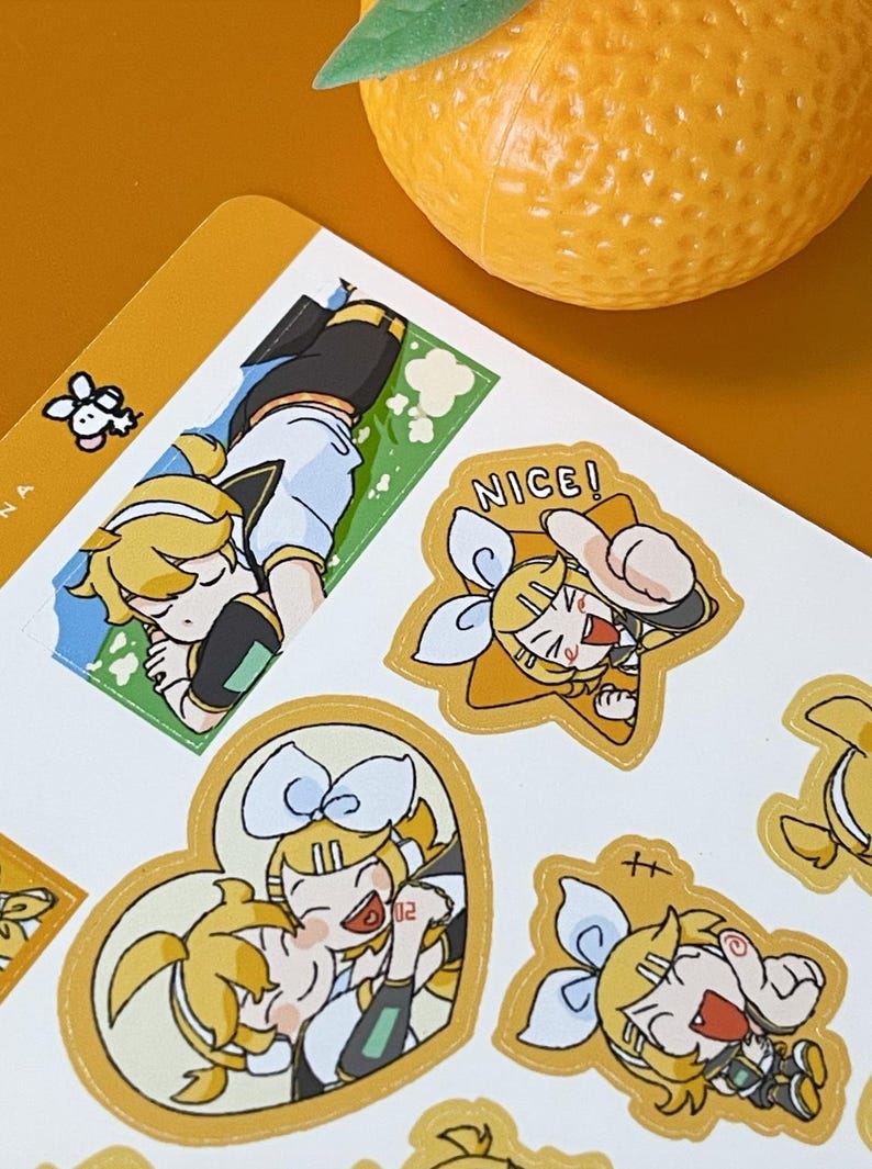 May include: Sheet of stickers featuring anime-style illustrations of a character with yellow hair and a blue bow. The stickers have a gold border and include the word "NICE!". An orange fruit sits in the background.