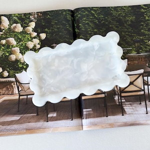 May include: A rectangular tray with a scalloped edge, crafted from a translucent, milky white material. The surface features a subtle, swirling pattern throughout, creating a soft, cloud-like appearance that catches the light across its wavy border.