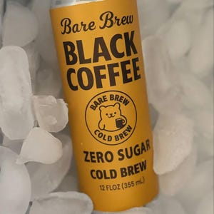 May include: A yellow can of Bare Brew Black Coffee, nestled in ice cubes. The can displays the product name and details in black text, including "Zero Sugar Cold Brew" and "12 FLOZ (355 ml)". A bear logo is also present.