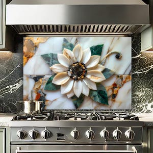 May include: A decorative kitchen backsplash featuring a large sunflower design. The sunflower is made of white and beige petals with a dark center, surrounded by green leaves. The backsplash is set against a marble background with a stainless steel range and hood.