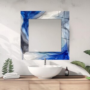 May include: A square wall mirror featuring a decorative border with an abstract fluid art pattern in shades of deep blue, grey, and white. The mirror is positioned above a white ceramic vessel sink and a light wood floating vanity cabinet.