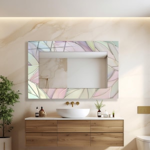 May include: Rectangular bathroom mirror with a decorative frame featuring a leaf-like pattern in pastel colors. The mirror is mounted above a wooden vanity with a white countertop and a round sink. The overall design is modern and elegant.