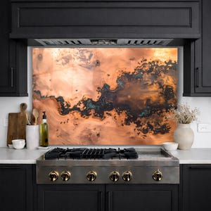 May include: A copper backsplash with a unique, abstract design in shades of brown, orange, and teal. The backsplash is installed above a stainless steel gas range in a modern kitchen setting.
