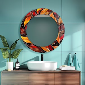 May include: A round decorative mirror with a colorful leaf design in shades of red, orange, and brown. The mirror is mounted on a teal tiled wall above a wooden vanity with a white sink. A potted plant and soap dispenser are on the vanity.