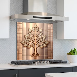 May include: A copper-toned kitchen backsplash with a raised, golden tree design. The tree features detailed leaves and branches, set against a textured background. The backsplash is installed above a stovetop and below a stainless steel range hood.