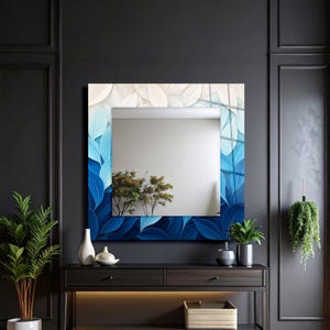 May include: A square wall mirror featuring a decorative border with a gradient leaf pattern that transitions from dark blue at the bottom to light blue and white at the top. The reflective center shows a clear view of a room with green plants.