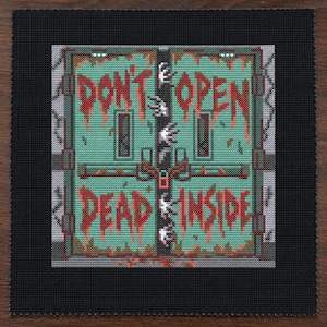 Puede incluir: Un bordado de punto de cruz cuadrado sobre tela negra que muestra una puerta doble de color verde azulado con el texto rojo "DON'T OPEN DEAD INSIDE" en estilo goteante. Manos blancas atraviesan la abertura central de las puertas con un candado rojo.