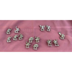 May include: A collection of small, silver-colored figurines, each depicting a fantastical creature in various poses. The figurines are arranged on a pink fabric surface, creating a whimsical display. The details of the figures are intricate.