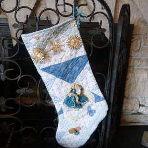 May include: A blue and white quilted Christmas stocking with a crocheted doll and gold buttons. The stocking is hanging on a black metal fireplace screen.