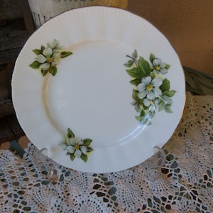 Puede incluir: Plato de cena de porcelana blanca con borde dorado y un diseño floral con flores blancas y hojas verdes.