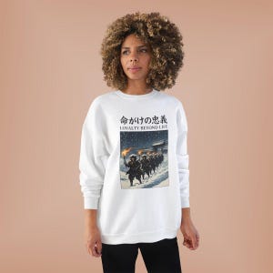 May include: White sweatshirt with a Japanese illustration of figures marching in the snow, holding torches. The text "LOYALTY BEYOND LIFE" is above the illustration in English and Japanese characters. The sweatshirt is worn by a person.
