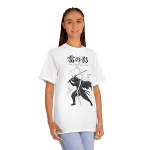 May include: White t-shirt featuring a black graphic of a samurai warrior with swords, lightning, and Japanese text. The text reads "Thunder Shadow" in English and Japanese characters. The shirt is a casual, comfortable style.