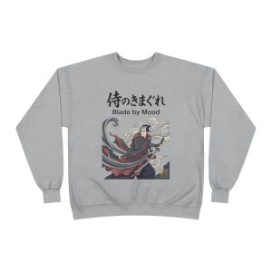 Może przedstawiać: Jasnoszara bluza z ilustracją w stylu japońskim przedstawiającą samuraja z mieczem. Grafika zawiera czarny napis "侍のきまぐれ Blade by Mood". Samuraj jest przedstawiony w kolorach czerwonym, czarnym i białym.