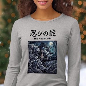 May include: A light gray long-sleeve shirt featuring a graphic of a ninja in a traditional pose, with a Japanese temple in the background. The text "忍びの掟 The Ninja Code" is printed above the graphic.