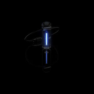 Peut inclure: Un objet en verre transparent, cylindrique, avec une lumière bleue verticale vive à l'intérieur. Il est relié à un cordon noir et repose sur une surface réfléchissante, créant un effet miroir. Le fond est noir.
