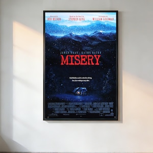 Op de afbeelding: Een ingelijste filmposter voor "Misery" met James Caan en Kathy Bates. De poster toont een besneeuwd berglandschap met een huis. De titel "Misery" is rood. Regie: Rob Reiner.