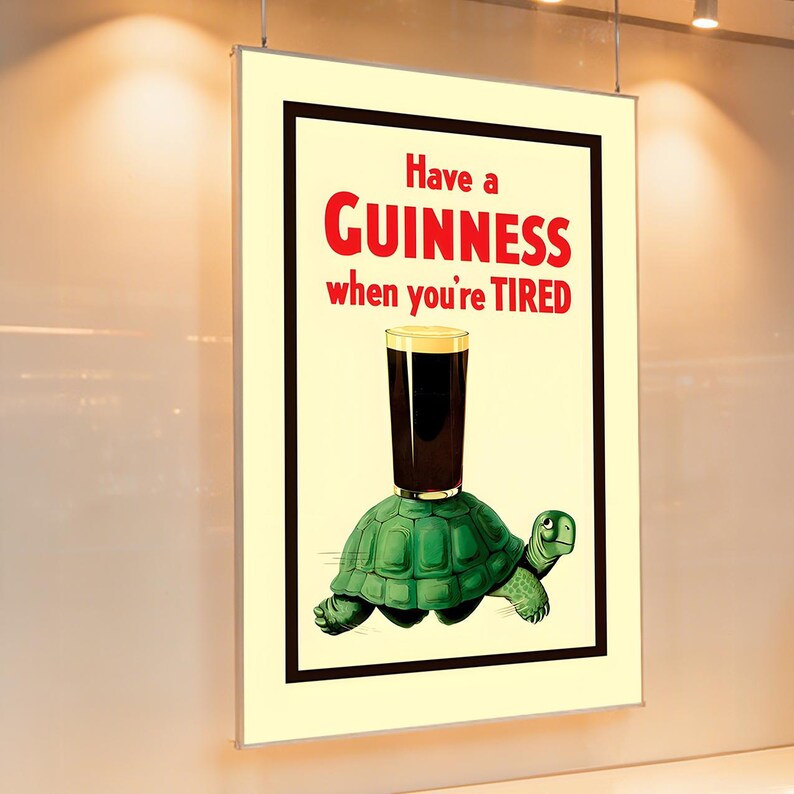 May include: A vintage Guinness advertisement featuring a cartoon turtle carrying a pint of Guinness stout. The text reads "Have a Guinness when you're TIRED" in red letters. The image is framed in black and set against a cream background.