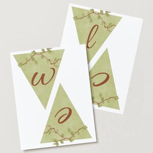 May include: Two white triangular cards with the letters "w", "e", and "c" in a brown script font. Each triangle has a light green watercolour background and is decorated with a leafy vine.