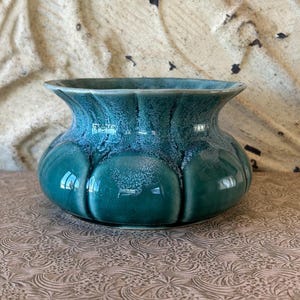 Könnte beinhalten: Eine türkisfarbene Keramikvase mit rundem Körper und ausgestelltem Rand. Die Vase hat ein strukturiertes, geripptes Design an der Außenseite. Die Farbe ist ein tiefes Türkis mit helleren blauen Akzenten, die einen Marmoreffekt erzeugen. Die Vase ist ein dekorativer Gegenstand.