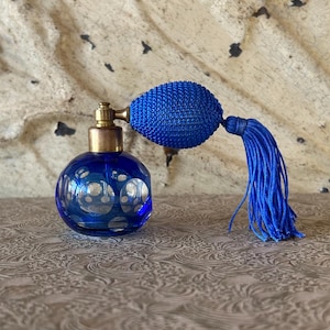 May include: A vintage cobalt blue perfume bottle with a bulb atomizer and tassel. The round glass bottle features a cut glass design. The atomizer is a matching blue color with a gold-colored metal top.