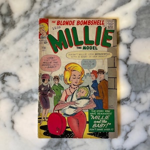 Puede incluir: Una portada de cómic vintage con una mujer con un vestido rojo sosteniendo un bebé. La portada se titula "The Blonde Bombshell Millie The Model" y presenta el texto "The story you have demanded! "Millie and the Baby!" Don't dare miss it!"