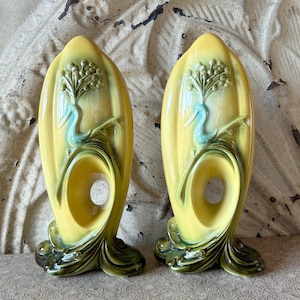 Puede incluir: Par de jarrones de cerámica amarilla vintage con diseño de pavo real. Los jarrones tienen forma curva con una gran abertura y base verde. El diseño del pavo real es en tonos verdes y azules. Los jarrones están sobre una superficie estampada.