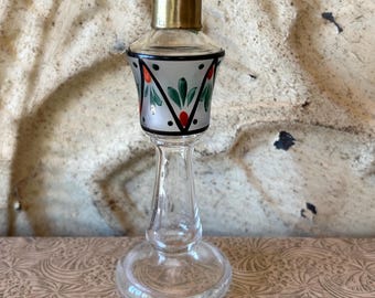 May include: A clear glass bottle with a gold top and a painted design of green leaves and red flowers. The bottle has a clear glass base.
