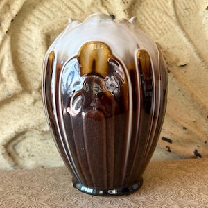 May include: A decorative ceramic vase with a white top and a dark brown body. The vase has a ribbed design and a glossy finish. The vase is sitting on a patterned surface.