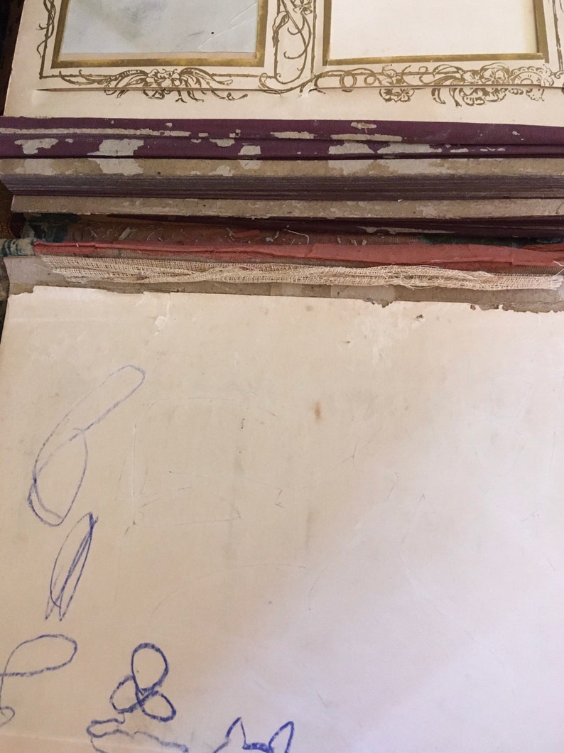 Puede incluir: Primer plano de una p&aacute;gina blanca en blanco con garabatos de l&aacute;piz azul. La p&aacute;gina es parte de un &aacute;lbum de fotos vintage con una cubierta de cuero marr&oacute;n.