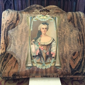 Puede incluir: Un &aacute;lbum de fotos vintage con una cubierta de madera y un dise&ntilde;o floral decorativo. La cubierta presenta un retrato de una mujer con un vestido azul y blanco con un ramo de flores.