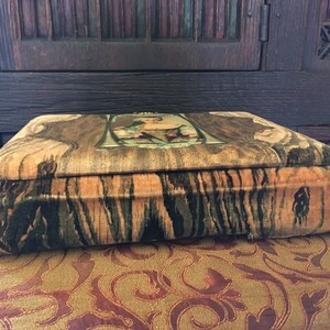 Puede incluir: Una caja vintage cubierta de terciopelo con un patr&oacute;n de veta de madera y un dise&ntilde;o floral en la parte superior. La caja est&aacute; cerrada y se encuentra sobre una superficie estampada.