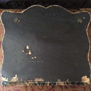 Puede incluir: La parte posterior de un marco de fotos vintage cubierto de terciopelo verde oscuro con un respaldo de cart&oacute;n negro. El marco tiene un borde superior festoneado y dos ganchos met&aacute;licos en la parte posterior para colgar.