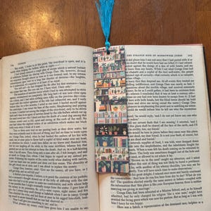 May include: A colorful bookmark with a blue tassel, featuring a repeating pattern of bookshelves and potted plants. The bookmark is placed in an open book with text visible on the pages, creating a cozy reading scene.