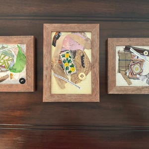 Puede incluir: Tres collages de técnica mixta enmarcados. Cada marco cuadrado es de madera marrón claro. Los collages presentan varias texturas, incluyendo papel, tela y elementos botánicos. Fragmentos de texto son visibles en cada pieza, con botones y cintas.