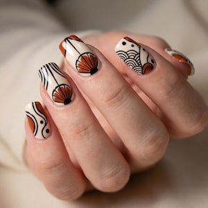 May include: A hand with long, almond-shaped nails. Each nail is painted with a unique design in cream, black, and burnt orange. The designs include geometric patterns and stylized shell motifs, creating a cohesive and artistic look.