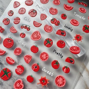 May include: A clear sticker sheet featuring numerous red tomato illustrations in various forms, including whole tomatoes, slices, and wedges. The sheet includes printed text in a cursive font with the words Pretty, Cute, Tomato, lovely, and Sweet.