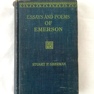 May include: A dark blue book with the title "Essays and Poems of Emerson" and the author "Stuart P. Sherman" printed on the cover. The book has a decorative border at the top and a small logo in the center.