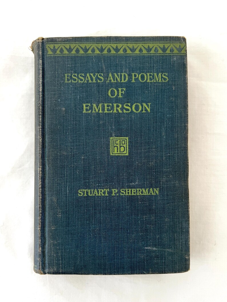 May include: A dark blue book with the title "Essays and Poems of Emerson" and the author "Stuart P. Sherman" printed on the cover. The book has a decorative border at the top and a small logo in the center.