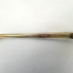 K&ouml;nnte beinhalten: Nahaufnahme einer Brille mit hellfarbenem Rahmen. Der Text "NO 1022 FRANCE" ist auf dem B&uuml;gel der Brille zu sehen. Die Brille hat ein klassisches Design.