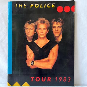 May include: A black and white promotional poster for The Police's 1983 tour. The poster features a photo of the band members, Sting, Andy Summers, and Stewart Copeland, with the band's name and tour dates in red and white text.