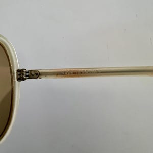 K&ouml;nnte beinhalten: Eine wei&szlig;e Keramik-Tasse mit schwarzem Henkel und dem Text "But First, Coffee" in fetter, schwarzer Schrift. Die Tasse steht vor einem verschwommenen Hintergrund, der eine gem&uuml;tliche Umgebung suggeriert. Die Tasse ist etwa 10 cm hoch.