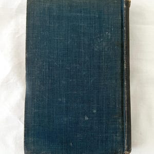 May include: A dark blue hardcover book with a textured fabric cover. The book has a spine with gold lettering.