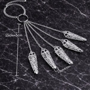 May include: Silver-toned finger armor jewelry with intricate filigree design. The set includes a ring connected to five finger covers by chains. Each finger cover is 1.5cm (0.59in) long. The total length is 20cm (7.87in).