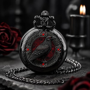 Peut inclure: Une montre de poche noire présentant une illustration détaillée de corbeau centrée sur un fond circulaire à motifs rouges et noirs. Le boîtier de la montre présente des gravures complexes et quatre petits accents rouges. Une chaîne en métal noir est fixée.