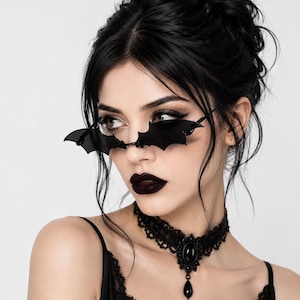 Puede incluir: Gafas de sol negras con monturas en forma de alas de murciélago, combinadas con un collar gargantilla de encaje negro que incluye una piedra negra ovalada central y un colgante negro en forma de lágrima, sobre una camiseta negra sin mangas.