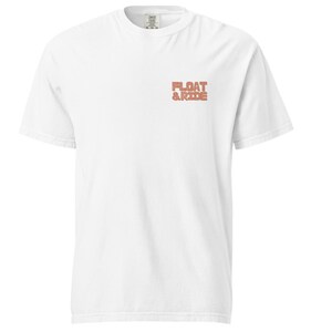 May include: A white short-sleeved t-shirt with the text "FLOAT & RIDE" in a coral-colored, blocky font on the upper left chest. The shirt has a crew neck and a relaxed fit.