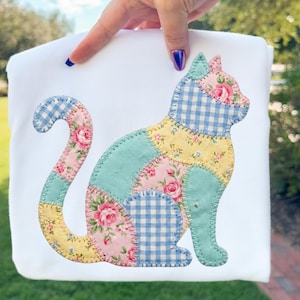 May include: White fabric with a patchwork cat design. The cat is composed of various fabric patterns, including floral, gingham, and solid colors in pink, blue, yellow, and green. The cat is in a seated position.
