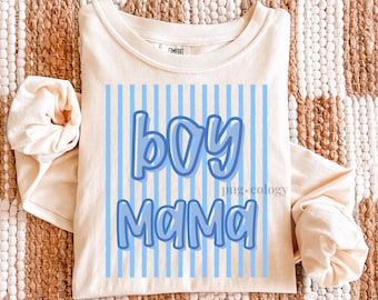 May include: Cream-colored long-sleeved shirt with the text "boy Mama" in light blue, set against a background of vertical blue stripes. The shirt is made of a soft material.
