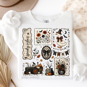May include: White sweatshirt with a collection of Halloween-themed illustrations. Designs include a goose in a witch hat, a tractor with pumpkins, floral arrangements, and the text "spooky vibes".